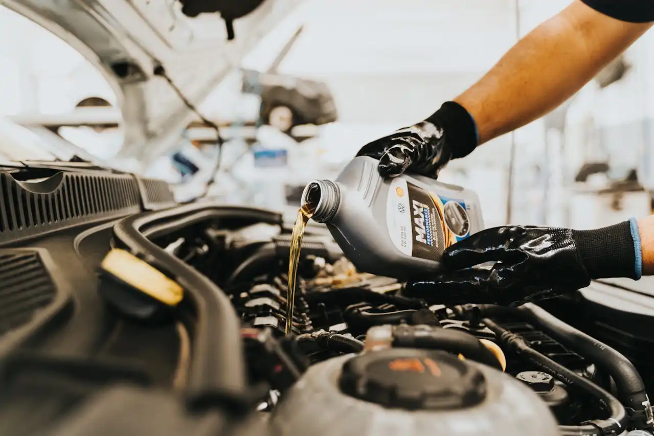 Mecánico vertiendo aceite de motor en un coche durante un mantenimiento, usando guantes protectores.